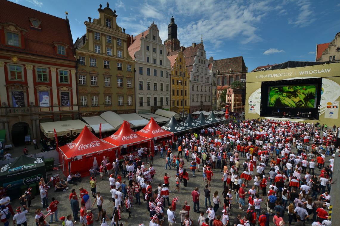 A stock image featuring a crowded outdoor inner city area with multiple branded gazebos in the center