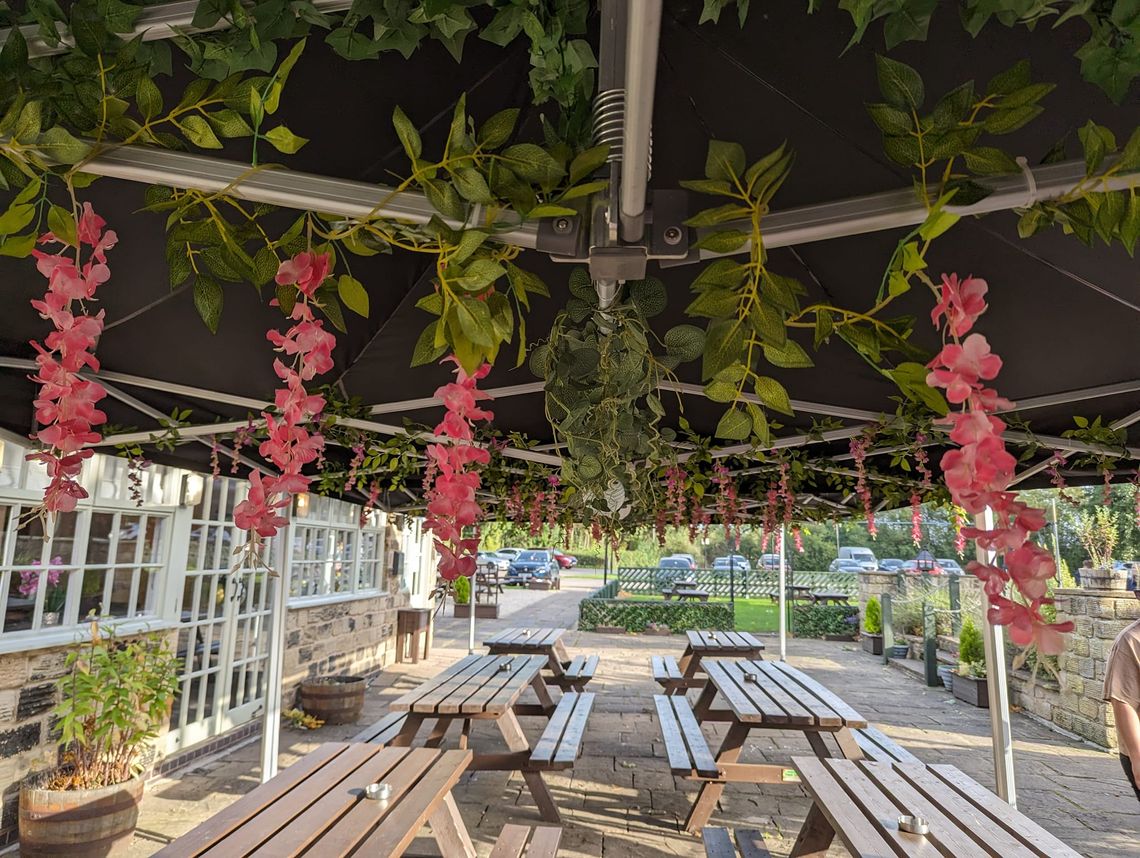 The underside of a pop up gazebo outside a British pub that has been decorated with flowers and lanterns