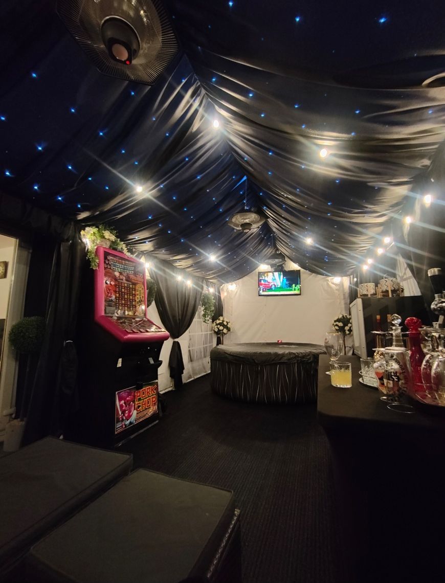 An internal view of a decorated garden marquee with lining and furniture at night time illuminated by lights