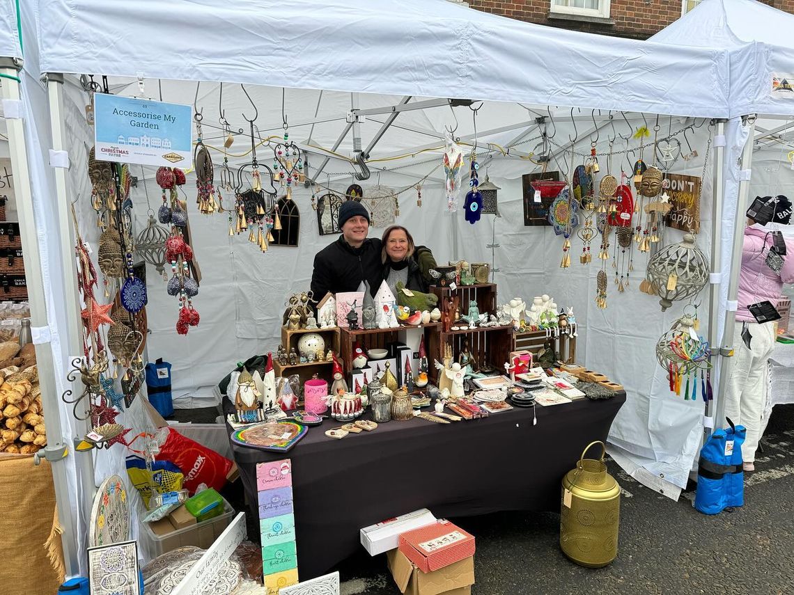 A man and a woman stand beneath a white gazebo selling products