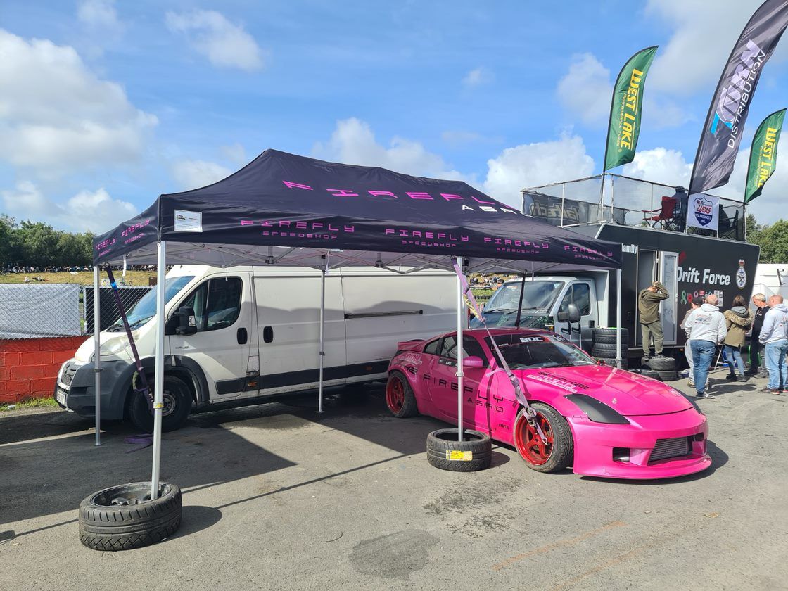 A bright pink drift car rests beneath a pop-up motorsport shelter