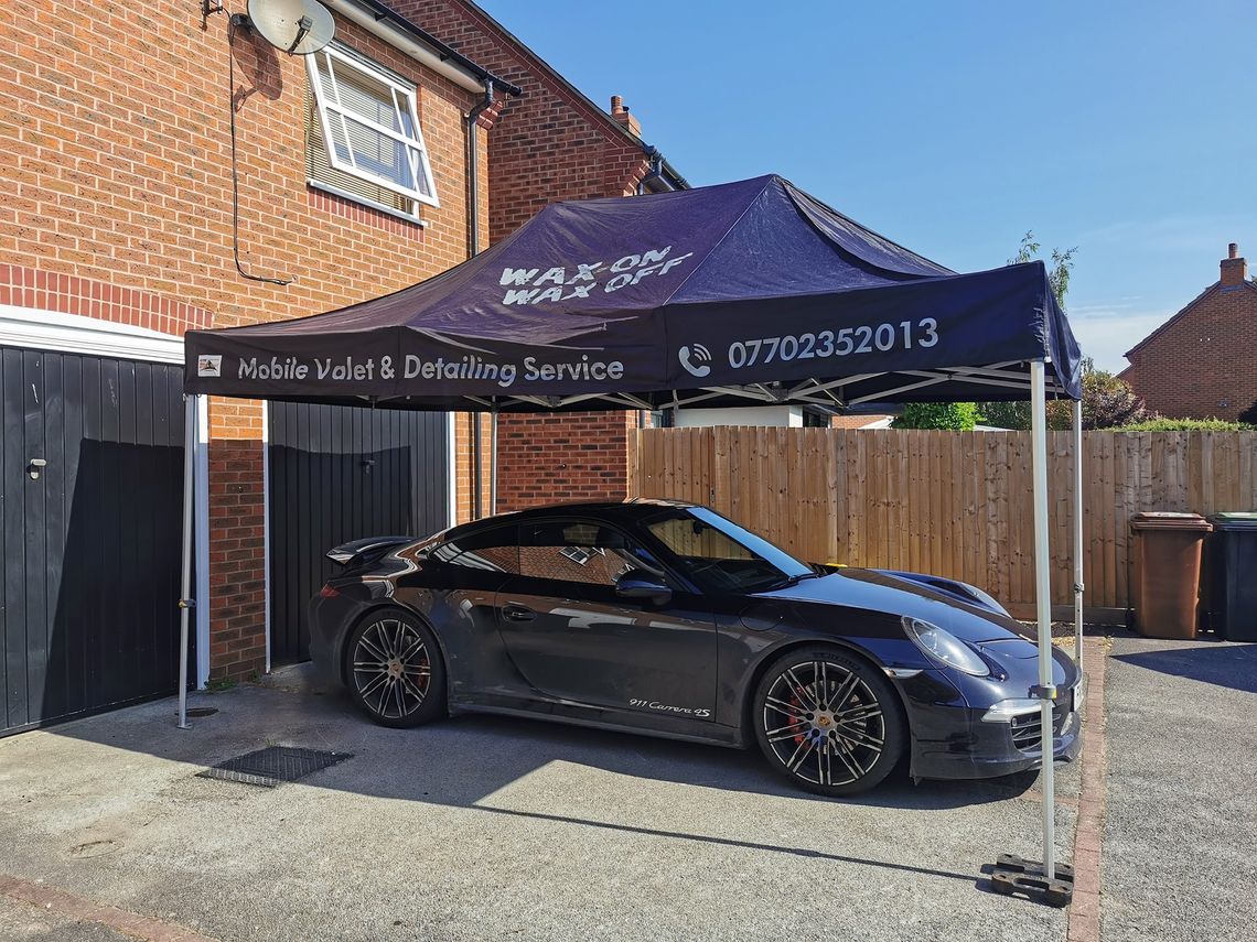 A porsche 911 sits beneath a mobile valeting pop-up shelter