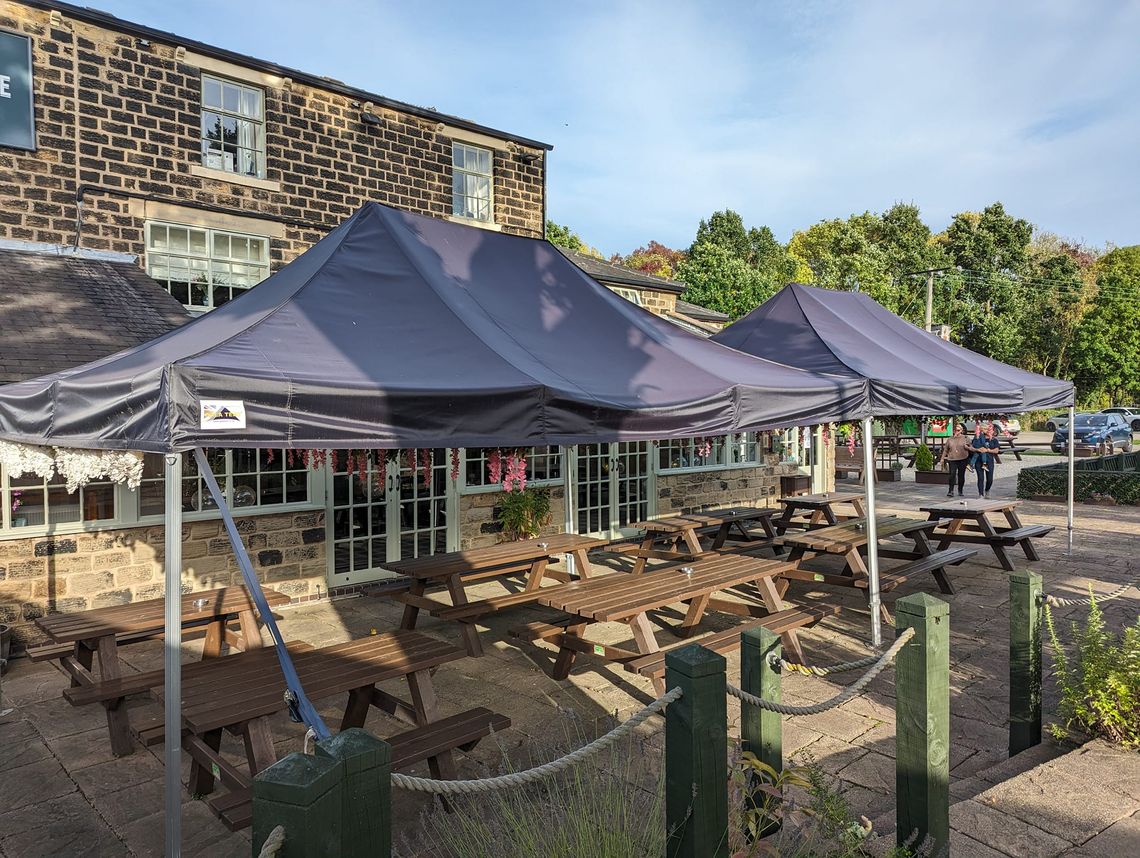 2 pop up[ gazebos covering some benches in a pub's beer garden