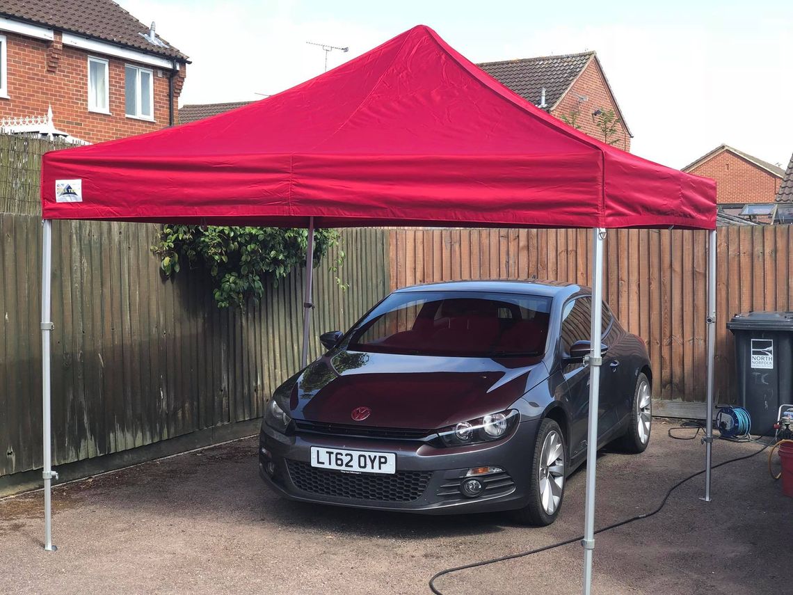 A black car beneath a fully erected compact gazebo