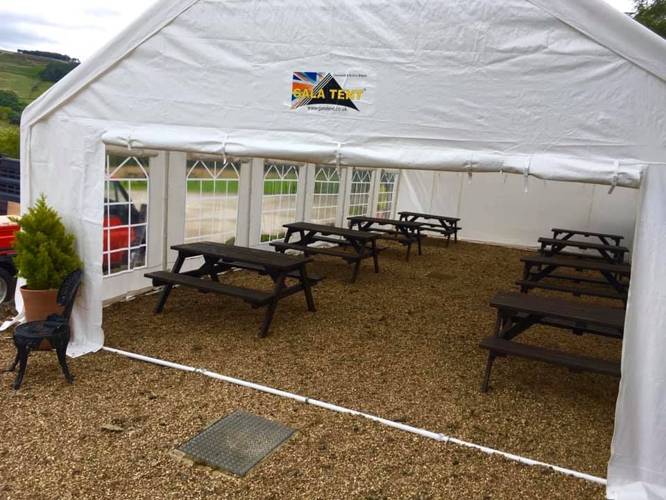 A white gala tent marquee sheltering outdoor benches in a pub garden