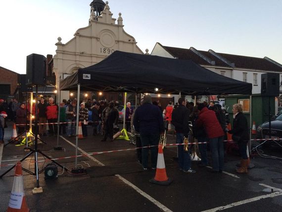 A black gazebo being used as shelter for a brass band
