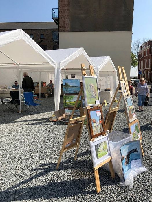 A white marquee being used as shelter for selling paintings in at a market