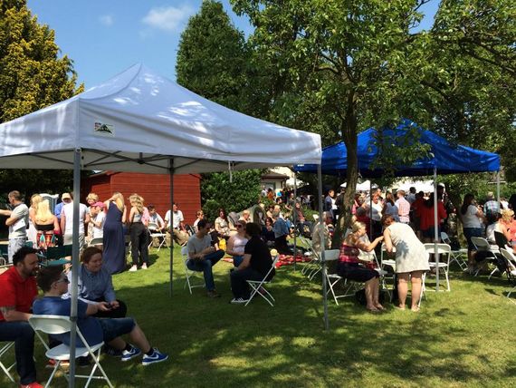 A white gazebo in the foreground with a blue gazebo in the background at a sunny outdoor event