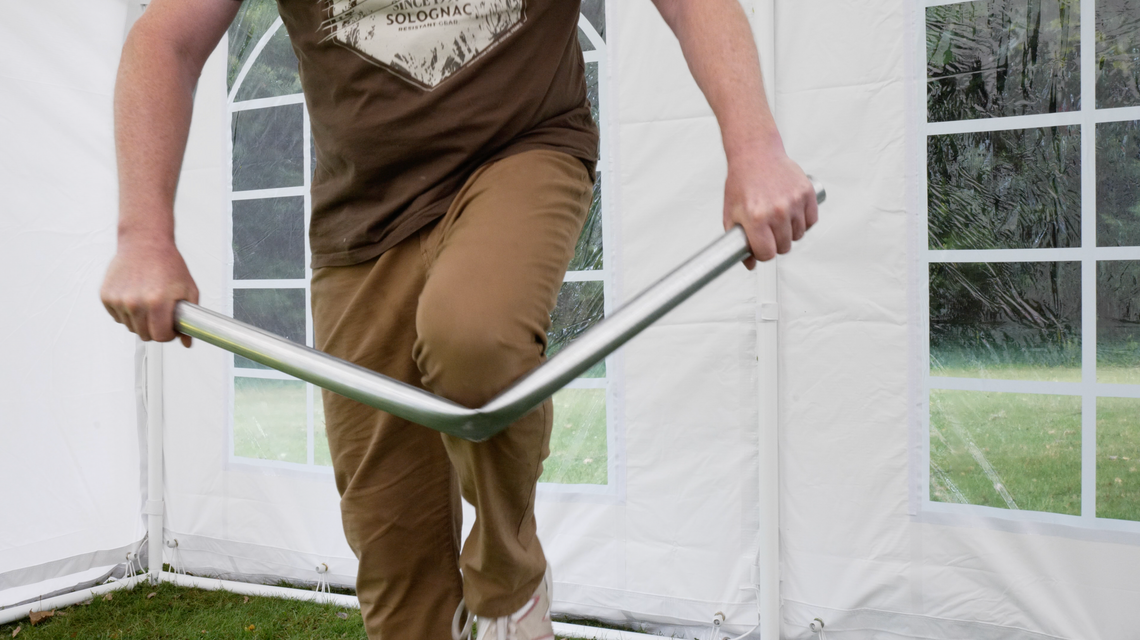 The weakness of a marquee pole by House of Tents being demonstrated by being bent beneath the owner's knee